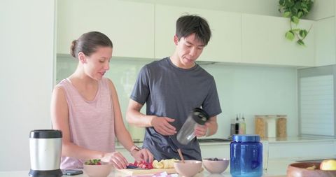 Couple preparing fresh fruit smoothie at bright modern kitchen island for healthy lifestyle