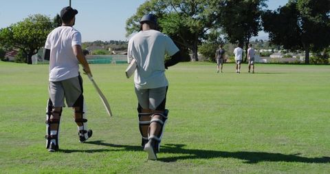 Cricket teammates walking across suburban green carrying bats and pads, teamwork focus