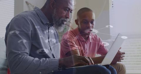 Older man guiding teen through online learning on laptop at home, mentoring moment