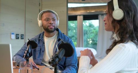 Co-hosts podcasting from cozy home studio wearing headphones and using mics with laptop