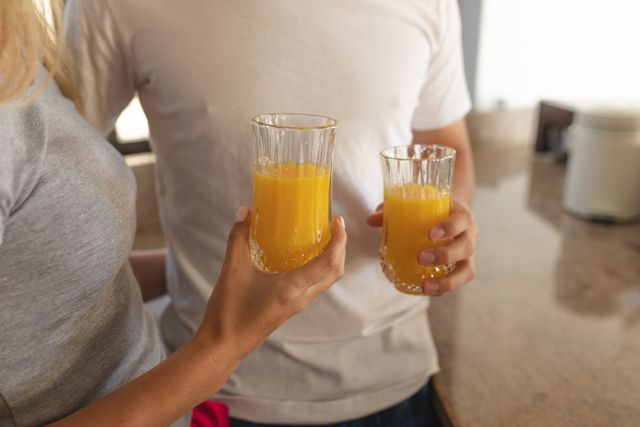 Caucasian couple spending time together, embracing holding glasses with orange juice. Social distancing and self isolation in quarantine lockdown during coronavirus Covid 19 pandemic.