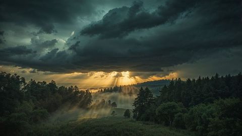 Dramatic Sunrise With Sun Rays Through Storm Clouds Over Misty Hills