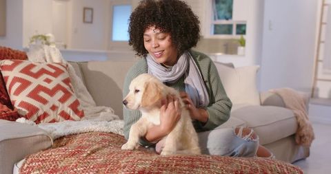 African American woman cuddling golden retriever puppy on cozy living room sofa