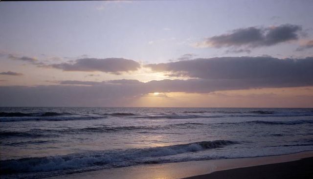 Glowing sunset sinking behind low clouds over calm ocean with foaming waves and wet sand