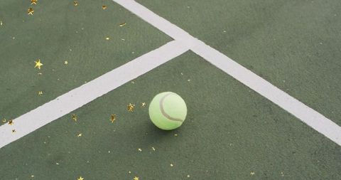Tennis ball on outdoor court with gold star confetti