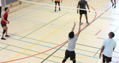 Indoor volleyball team playing competitive pickup match on multi-line gym hardwood court