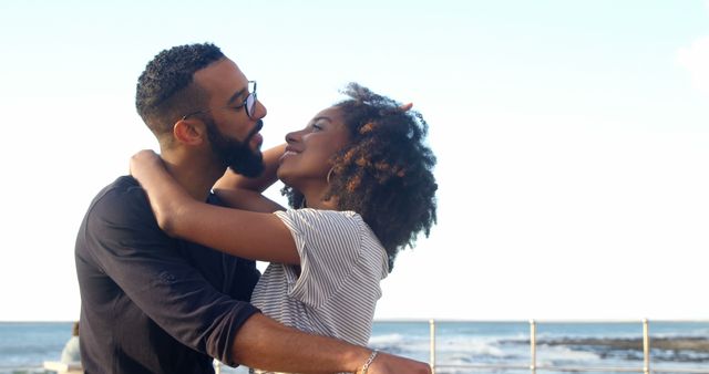 Romantic diverse couple embracing and smiling on sunny beach, copy space. Summer, vacation, romance, love, relationship, free time and lifestyle, unaltered.