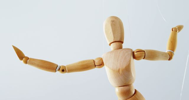 A wooden artist's mannequin is posed with arms outstretched against a plain background, with copy space. These mannequins are often used by artists for reference when drawing human figures.