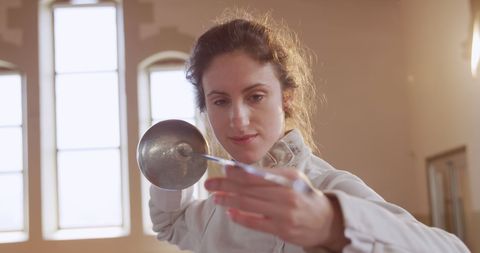 Focused Female Fencer Holding Sword in Training Hall