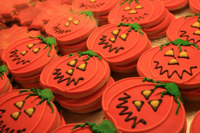 Assorted pumpkin-shaped cookies decorated with orange icing and spooky faces are arranged together. These vibrant and festive treats are perfect for Halloween-themed events, parties, and baking promotions. They create a playful and fun holiday atmosphere, making them ideal for advertisements, social media posts, and party invitations.
