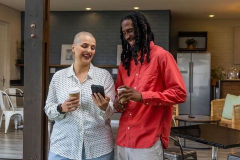 Friends sharing coffee and laughing while checking smartphone in modern kitchen lounge