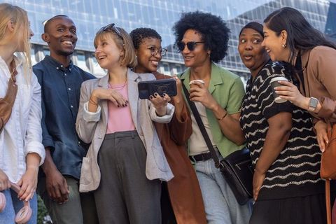 Multicultural group of young professionals laughing and sharing smartphone in urban plaza