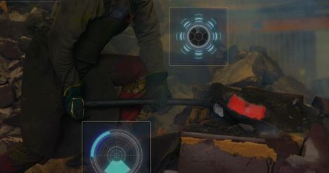 Crouching industrial worker using sledge on glowing metal in foundry with digital hud