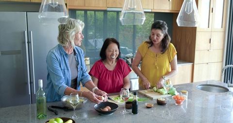 Multicultural women friends cooking together laughing while preparing fresh healthy meal