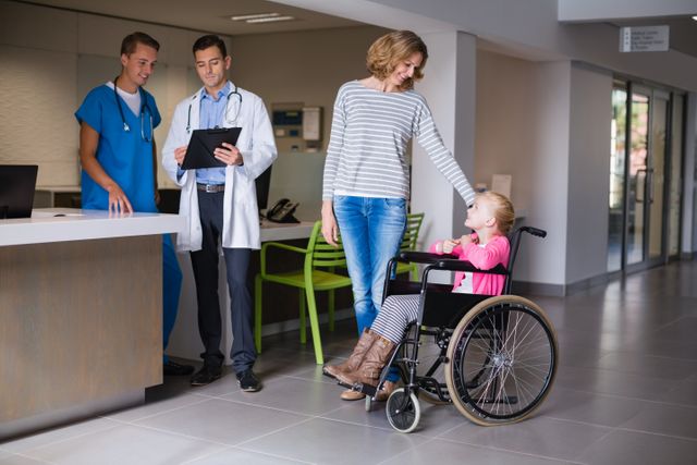Doctors discussing over clipboard and woman standing with disable girl in corridor