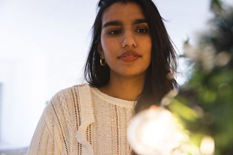 Woman admiring glowing ornament on evergreen branch during festive holiday season