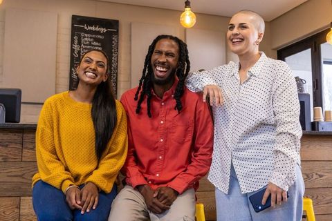 Diverse friends laughing at cozy cafe counter holding smartphone under warm pendant lights