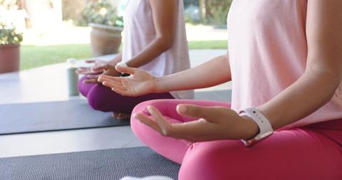 Women meditating on outdoor patio in pink leggings practicing mindfulness and yoga