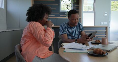 Young Couple Reviewing Documents with Tablet and Laptop in Kitchen