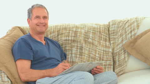 Retired Man Relaxing on Sofa Enjoying Crossword Puzzle