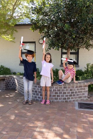 Kids celebrating graduation outdoors holding diplomas on brick courtyard planter