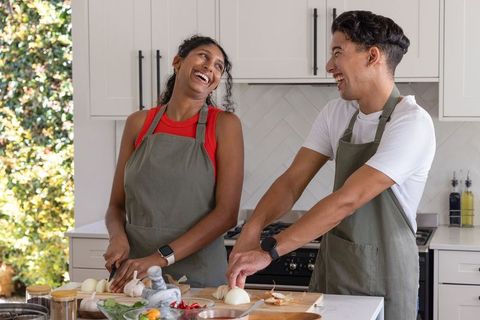 African american couple laughing and chopping vegetables together in sunlit modern kitchen