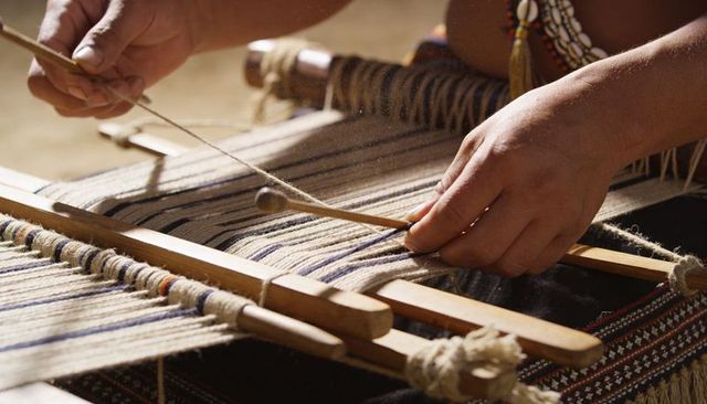 Sunlit artisan weaving on traditional loom guiding wooden shuttle for handmade textiles