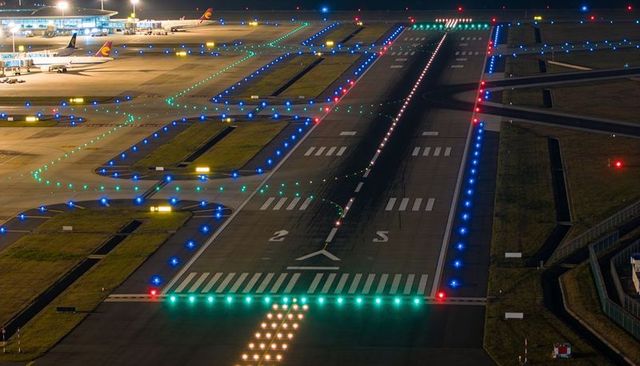 Illuminating runway 25 at night with green threshold and blue taxiway lights, airliners resting