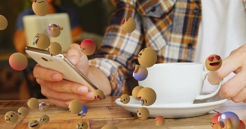 Woman using smartphone with flying emojis in coffee shop