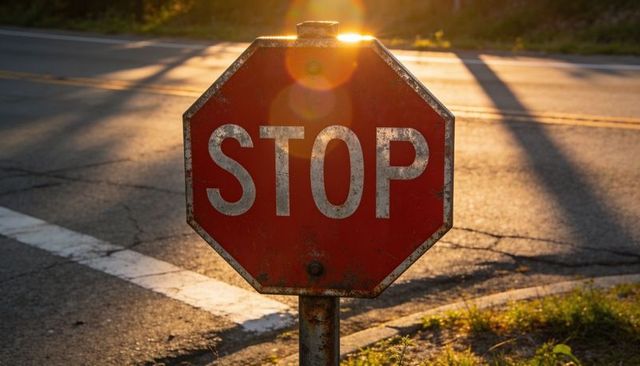 Weathered octagonal stop sign at roadside with rust and lens flare during golden hour