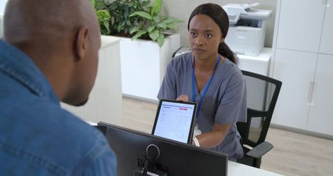 African american nurse presenting tablet with invoice to patient at clinic reception desk