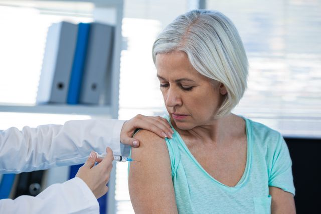 Senior woman receiving vaccination from healthcare professional in hospital. Perfect for articles on healthcare, elderly care, vaccination campaigns, and medical treatments.