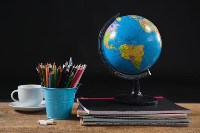 Colorful school supplies including a globe, colored pencils in a blue container, and stacked notebooks on a wooden table. Ideal for educational materials, back-to-school promotions, classroom decor, and learning resources.