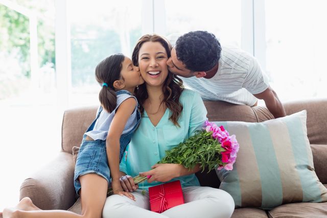 Woman receiving kiss from his husband and daughter in living room at home