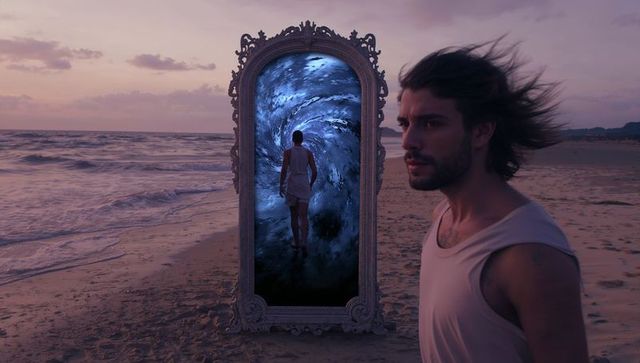Man in front of surreal vortex mirror on beach at dusk