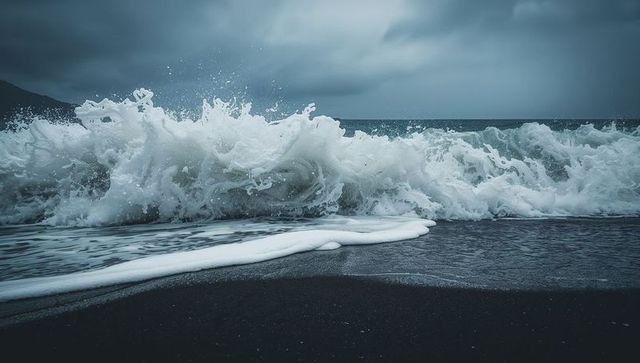 Crashing ocean wave on dark sand shore under overcast storm clouds with frothy surf