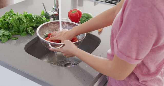 This image depicts the midsection of an Asian woman washing vegetables in a kitchen setting, emphasizing a healthy lifestyle at home. The focus on fresh produce and cleanliness makes it ideal for use in articles or advertisements related to healthy eating, home cooking, kitchen hygiene practices, and lifestyle blogs. It can also be used in standalone pieces highlighting home-life, wellness, and the importance of natural food preparation.