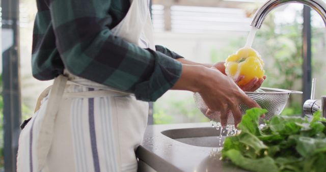 Hands washing yellow bell pepper and green lettuce at kitchen sink, showcasing fresh ingredients and home cooking. Ideal for use in articles or blogs on healthy eating, cooking tutorials, food hygiene tips, or organic lifestyle promotions.