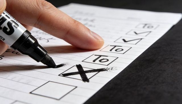 Hand marking checkbox with black marker on to-do list closeup, bold ink X and smudge
