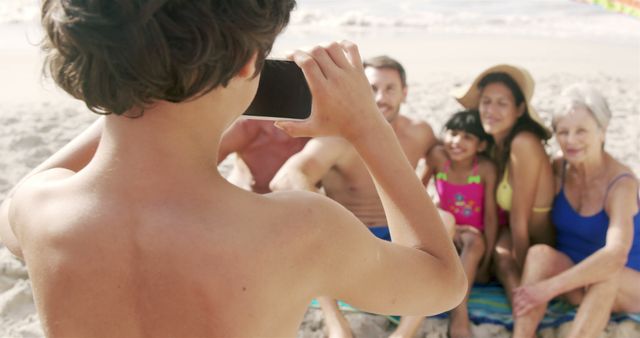 Boy happily taking a group photo of sitting family members on sandy beach. Ideal for themes around family vacations, outdoor activities, summer fun, travel destinations, and capturing memories. Suitable for travel and tourism marketing, family-oriented advertisements, and vacation planning content.