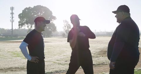 Mature coaches conversing and gesturing on dewy sports field at dawn team meeting