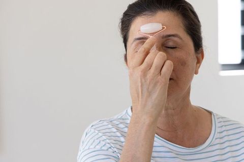 Mature asian woman using rose quartz facial roller for at-home skincare and relaxation