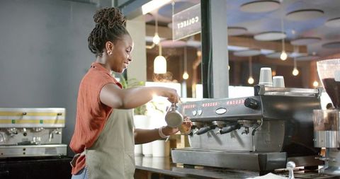 African woman barista pouring steamed milk into espresso at modern cafe with warm ambience