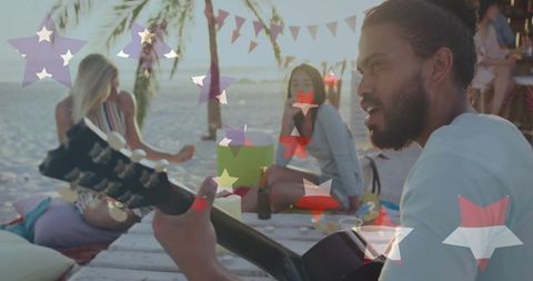 Bearded man playing acoustic guitar at beach party with friends, candles and palm trees