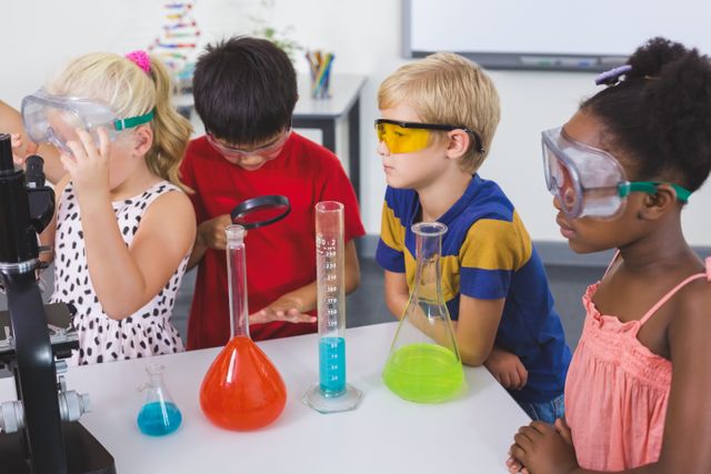 Group of children in a school laboratory engaged in a hands-on chemistry experiment, wearing safety goggles and focused on beakers filled with colorful liquids. Ideal for educational content, STEM programs, school advertising, and promoting hands-on learning experiences.
