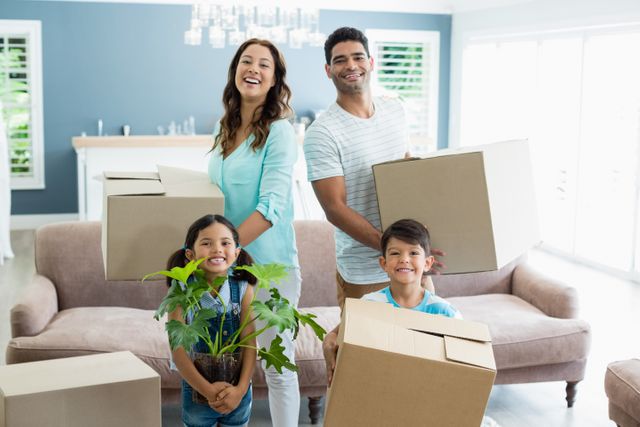 Happy family of four holding cardboard boxes and a plant in a bright living room. Parents and children smiling, indicating excitement and joy of moving into a new home. Ideal for use in real estate, home moving services, family lifestyle blogs, and advertisements promoting family-oriented products.