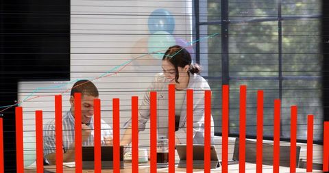 Two coworkers collaborating over laptops with finance charts and red data overlay