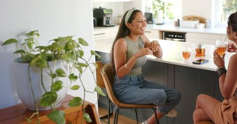Women chatting over tea at kitchen island, smiling and sharing morning chat