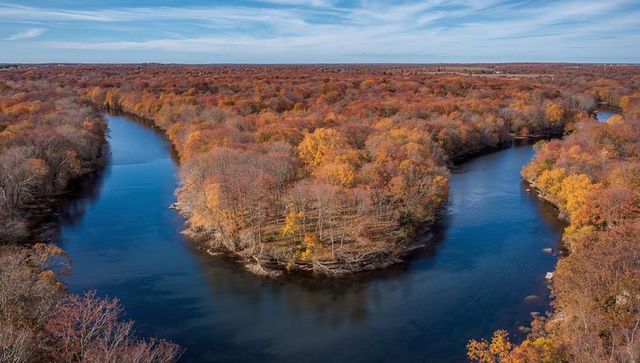 Autumn river winding around wooded peninsula with golden fall foliage and clear sky