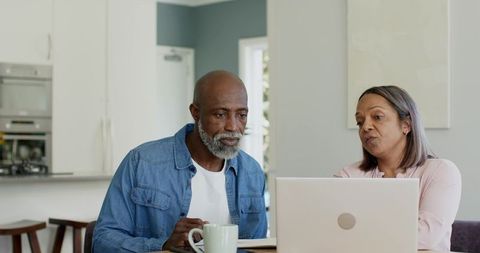 Senior couple using laptop in modern kitchen planning finances and exploring retirement